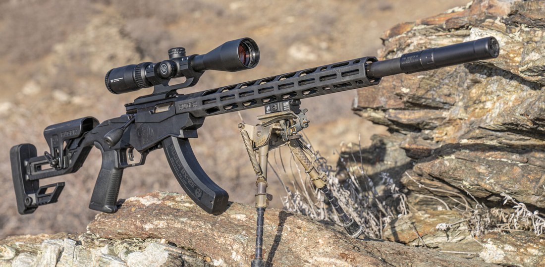 Figure 3 — A Ruger Precision Rimfire, scoped and suppressed — a stock photo of the type, not Jeff's rifle. The free-floated heavy barrel on a chassis is the reason this is the gun in the battery that can actu…