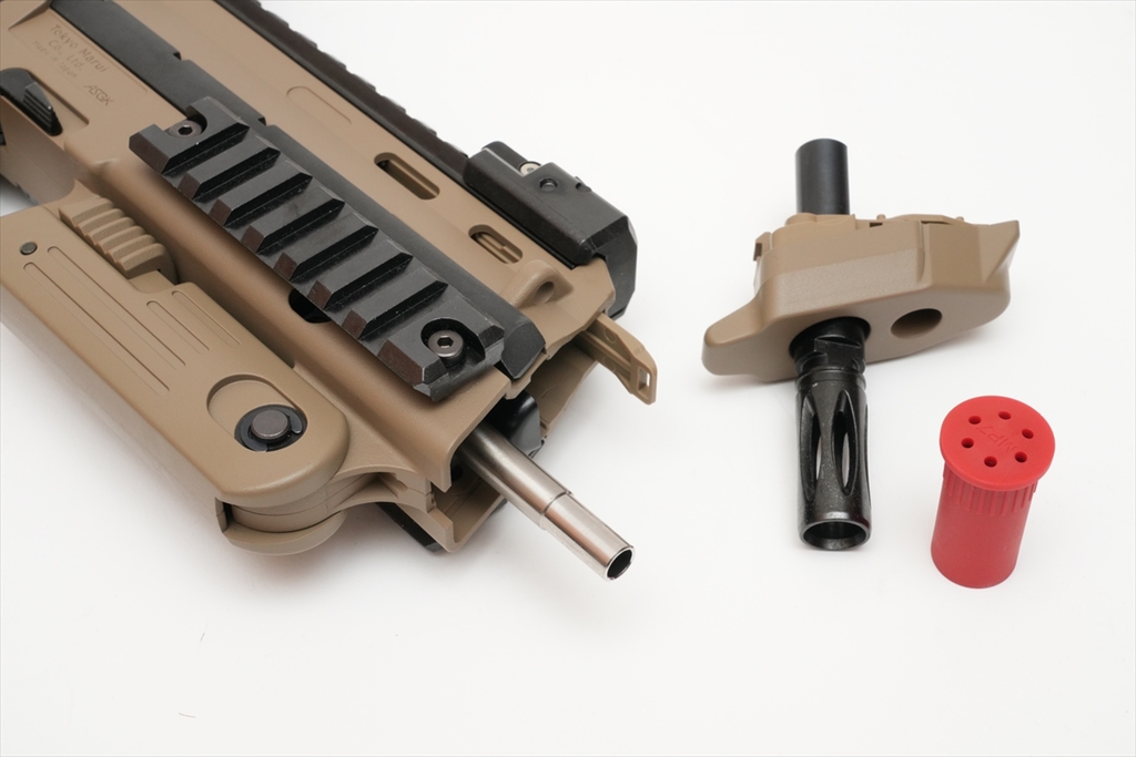 Figure 5 — An owner's Tokyo Marui electric MP7A1 in tan with the front cap removed, the stainless inner barrel exposed, and the replacement long inner barrel's front cap and flash hider beside it. Photo: ASCI…