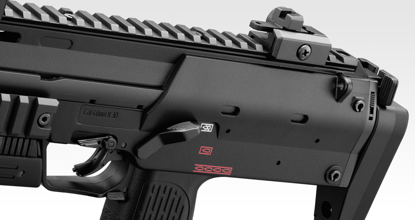 Figure 3 — The rear half of the Tokyo Marui gas gun from the left, stock collapsed, with the selector above the grip and the rear sight on the top rail. The bolt carrier runs inside this upper receiver; the s…