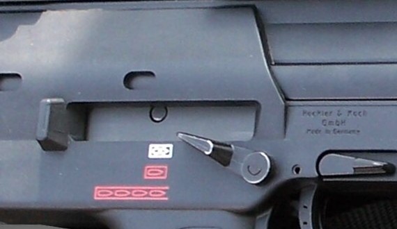Figure 3 — What a real MP7A1 carries behind its selector: H&K's company name and "Made in Germany" moulded into the receiver, the selector lever, and the three fire-mode pictograms, white for safe and red for…