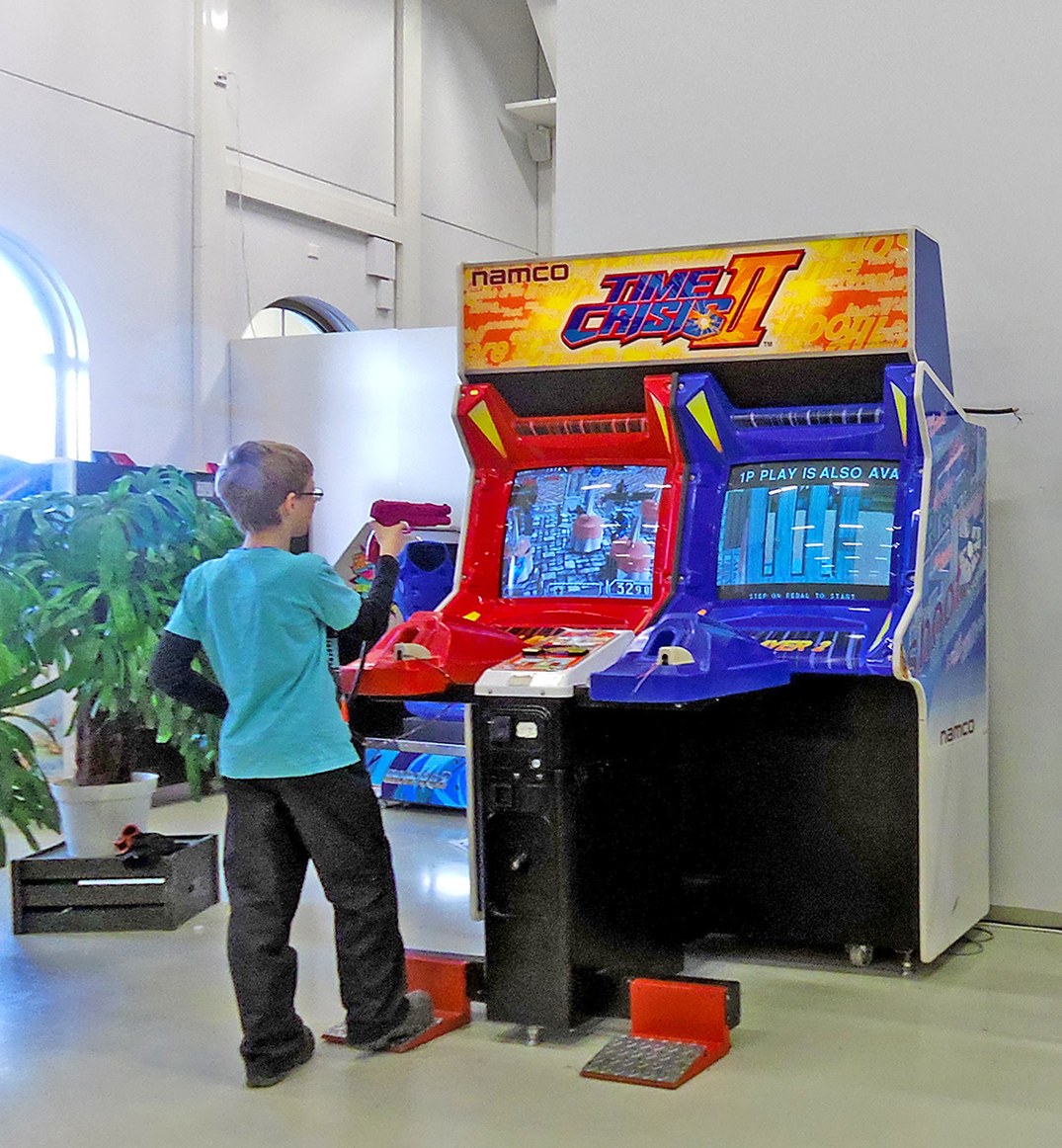 Figure 6 — A Time Crisis II twin cabinet in a Finnish shop, a player at the red gun with his foot on the pedal. Each player has a 1990s CRT, a holstered gun and an action pedal. Photo: Tiia Monto, Wikimedia C…