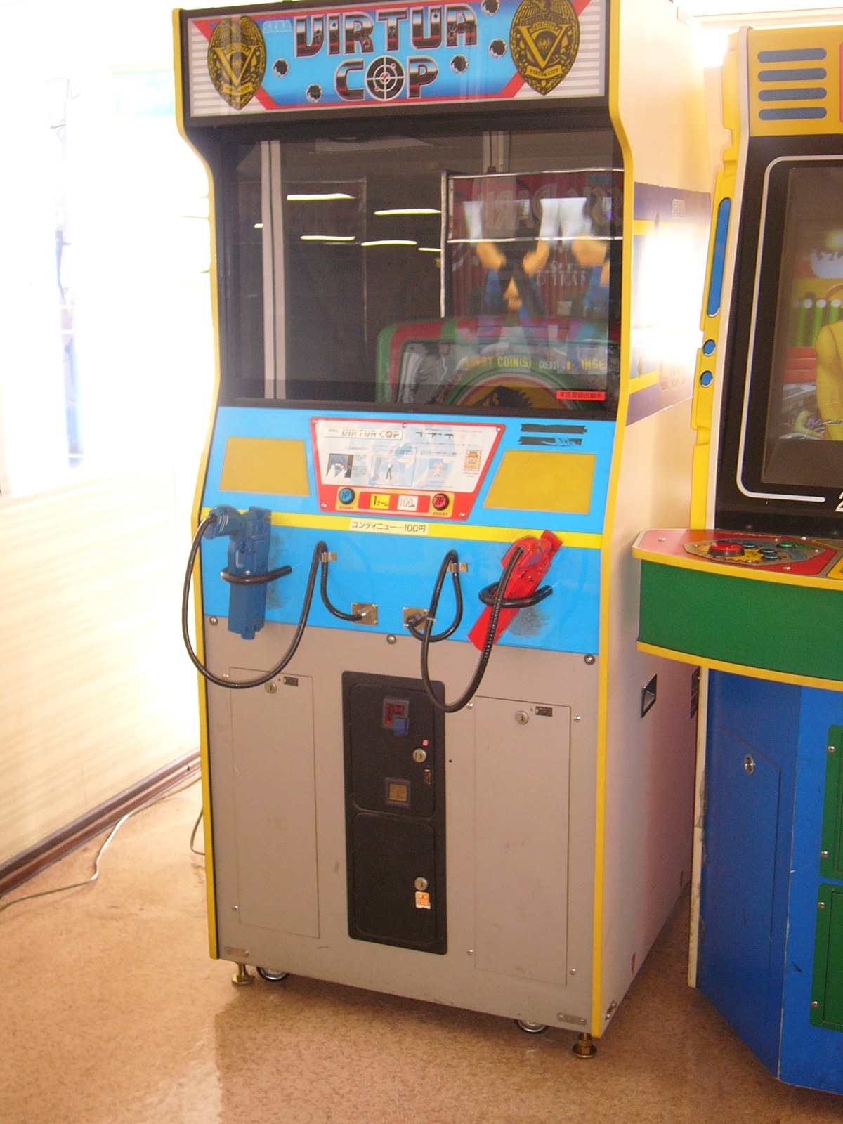 Figure 5 — A Virtua Cop cabinet with its two holstered guns, blue and red, on the control panel. Photo: Medalizm, Wikimedia Commons, CC BY 3.0.