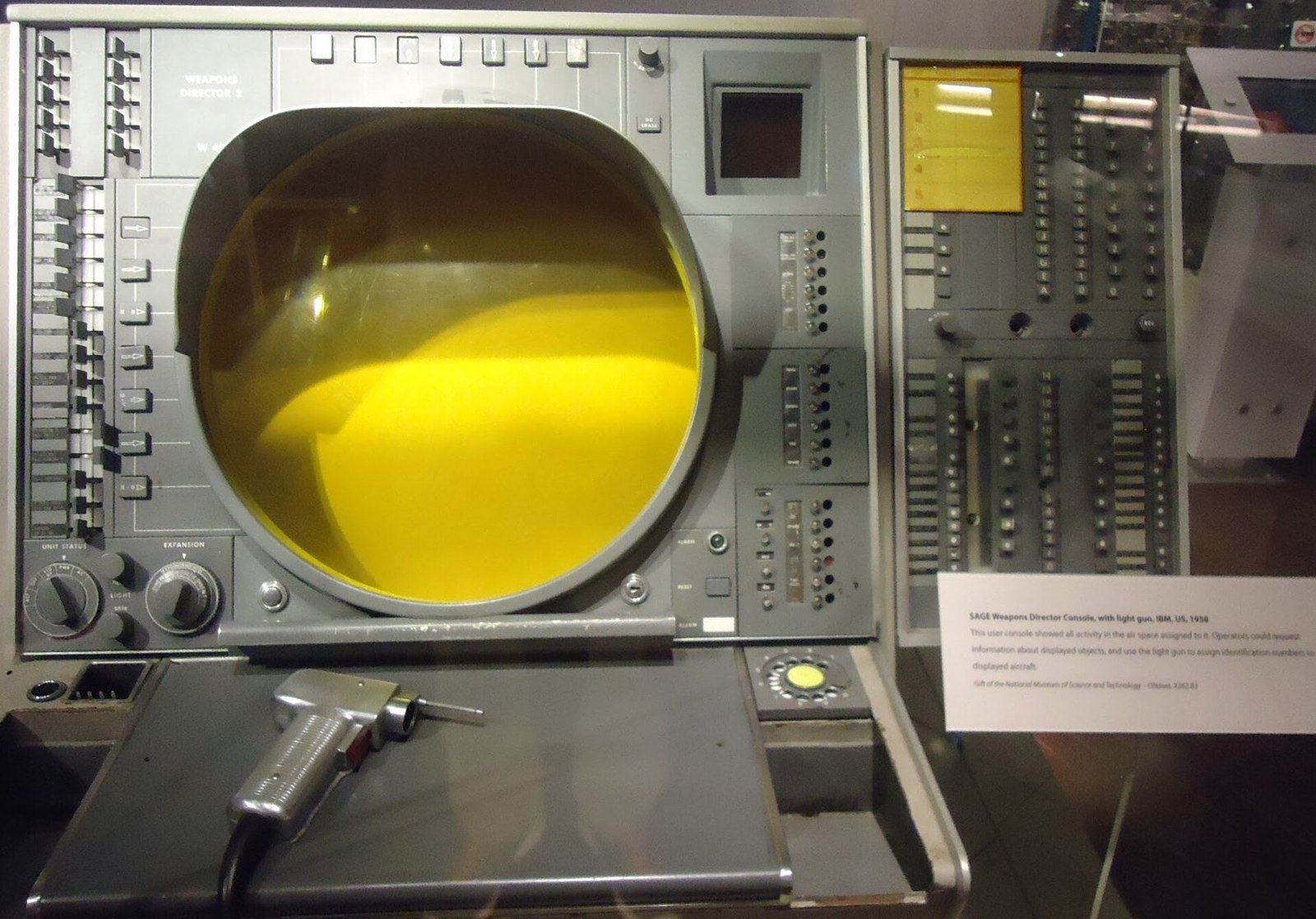 Figure 1 — The SAGE weapons director console of 1958 with its light gun resting on the shelf below the round yellow-phosphor display. The operator pointed the gun at a radar track on the screen and pulled the…