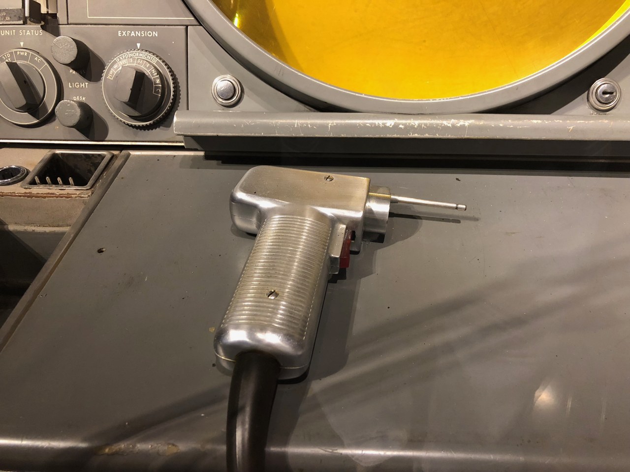 Figure 2 — The SAGE light gun close up, on the shelf of the weapons director console at the Computer History Museum. It is a pistol grip with a short tube for a barrel and a cable out of the butt; the operato…