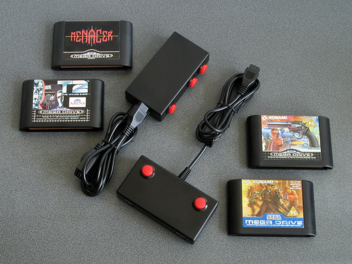 Figure 4 — Ben Ryves's two Mega Drive gun adaptors with the games he tested them on: the hand-held Menacer adaptor with its three buttons, and the Justifier adaptor. Photo: Ben Ryves, benryves.com.