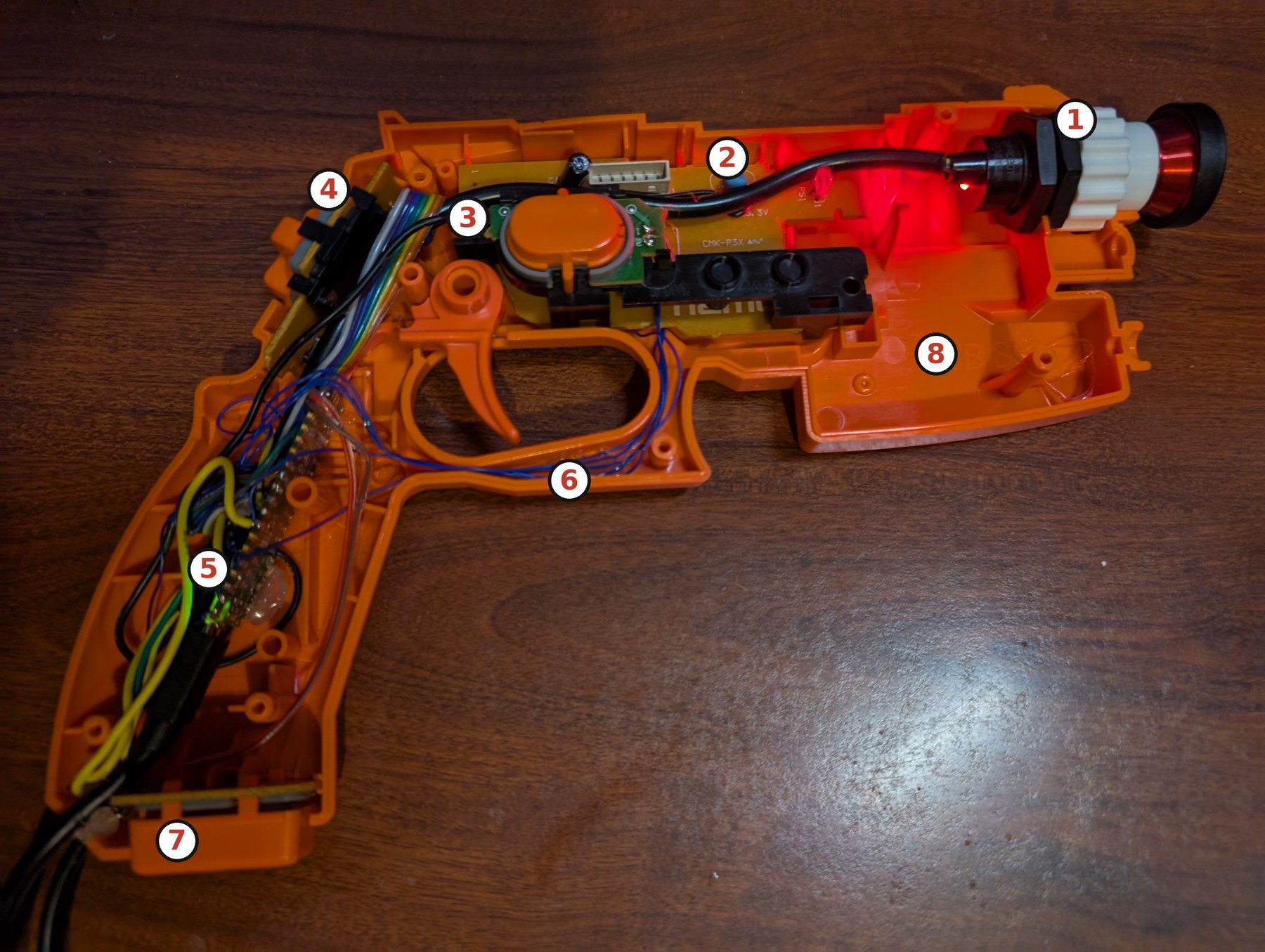 Figure 2 — The converted GunCon 2 open, with this volume's numbered key. 1: the IR camera in the white printed coupler, held to the muzzle tabs by hex nuts, with the red fisheye lens in front. 2: the original…