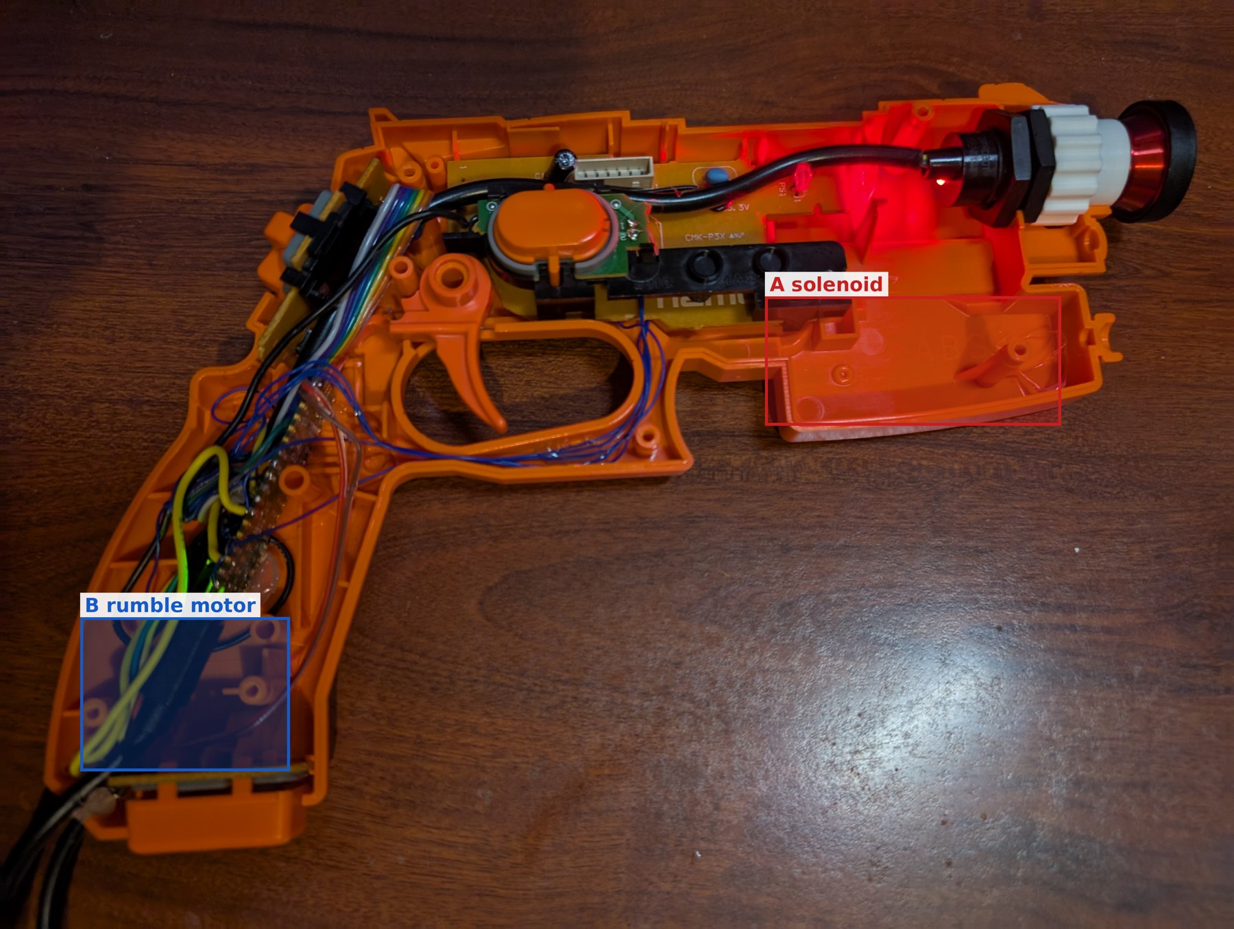 Figure 3 — The converted GunCon 2 with two candidate zones marked. A: the lower front of the slide ahead of the trigger guard, empty after the conversion and long enough for a small solenoid lying parallel to…