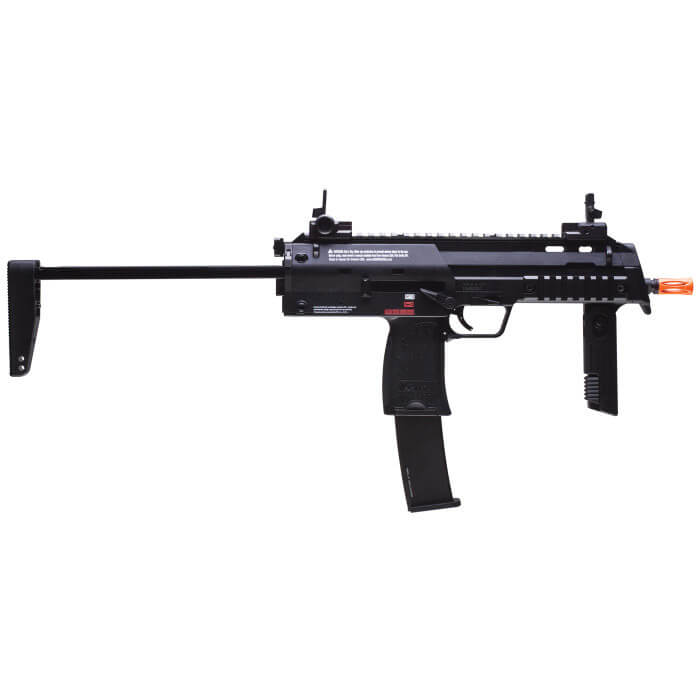 Figure 3 — The licensed Umarex H&K MP7 GBB airsoft rifle from the left, stock extended, with its 40-round magazine fitted and a blaze-orange muzzle. The receiver carries a printed warning block, the trademark…