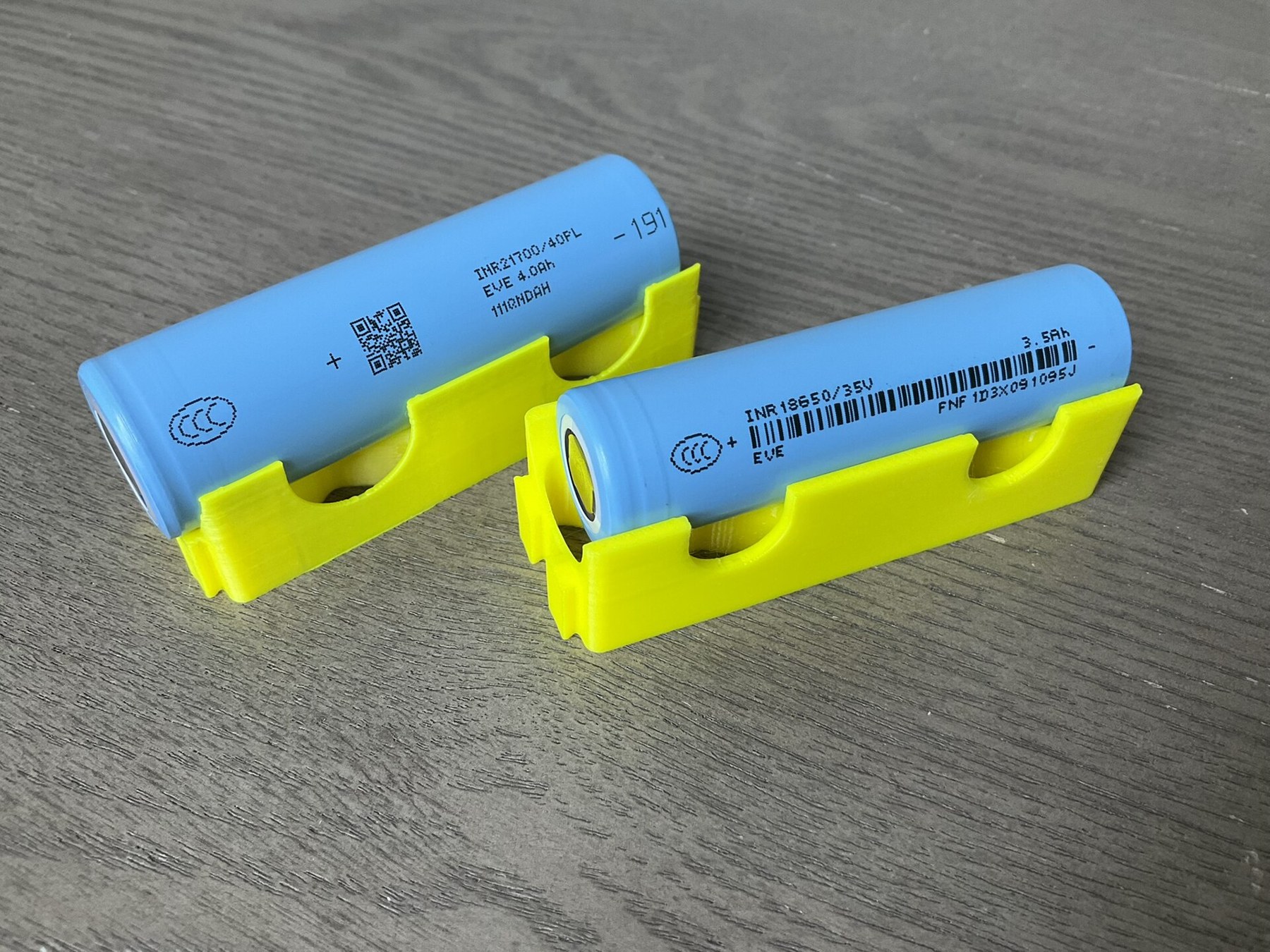 Figure 3 — An 18650 and a 21700 lithium-ion cell in printed holders: EVE INR18650/35V and INR21700/40PL. An 18650 is 18 mm by 65 mm; a 21700, 21 mm by 70 mm. Photo: Wikimedia Commons, Sevenethics, CC0.