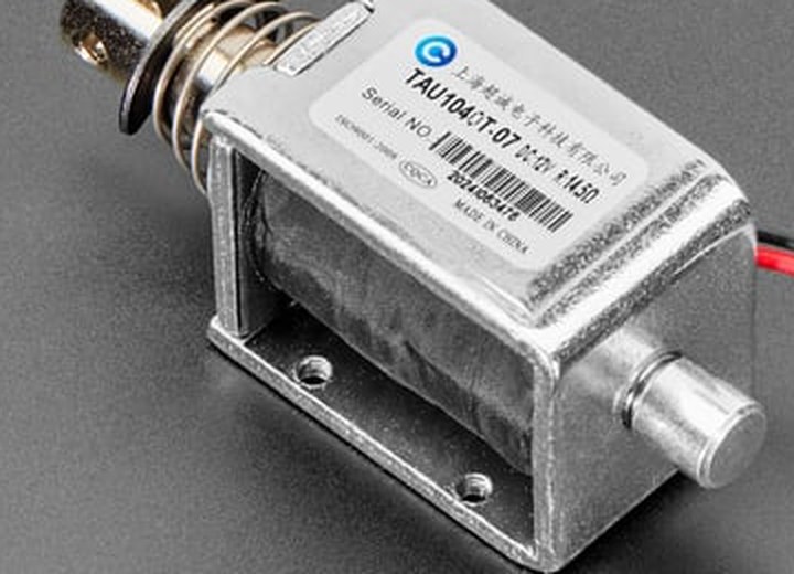 Figure 6 — The label on the Adafruit 413 solenoid, enlarged from the product photograph: "TAU1040T-07", "DC12V", a serial number, a Shanghai maker's name in Chinese, "ISO9001:2008" and "MADE IN CHINA". The la…