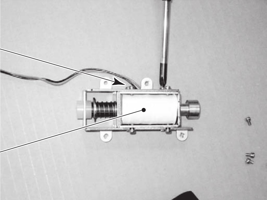 Figure 10 — The Ghost Squad solenoid removed from its assembly: a box-frame coil, the plunger's spring on the left and the plunger's end on the right. Photo from the Sega Ghost Squad manual (2004), page 95, vi…
