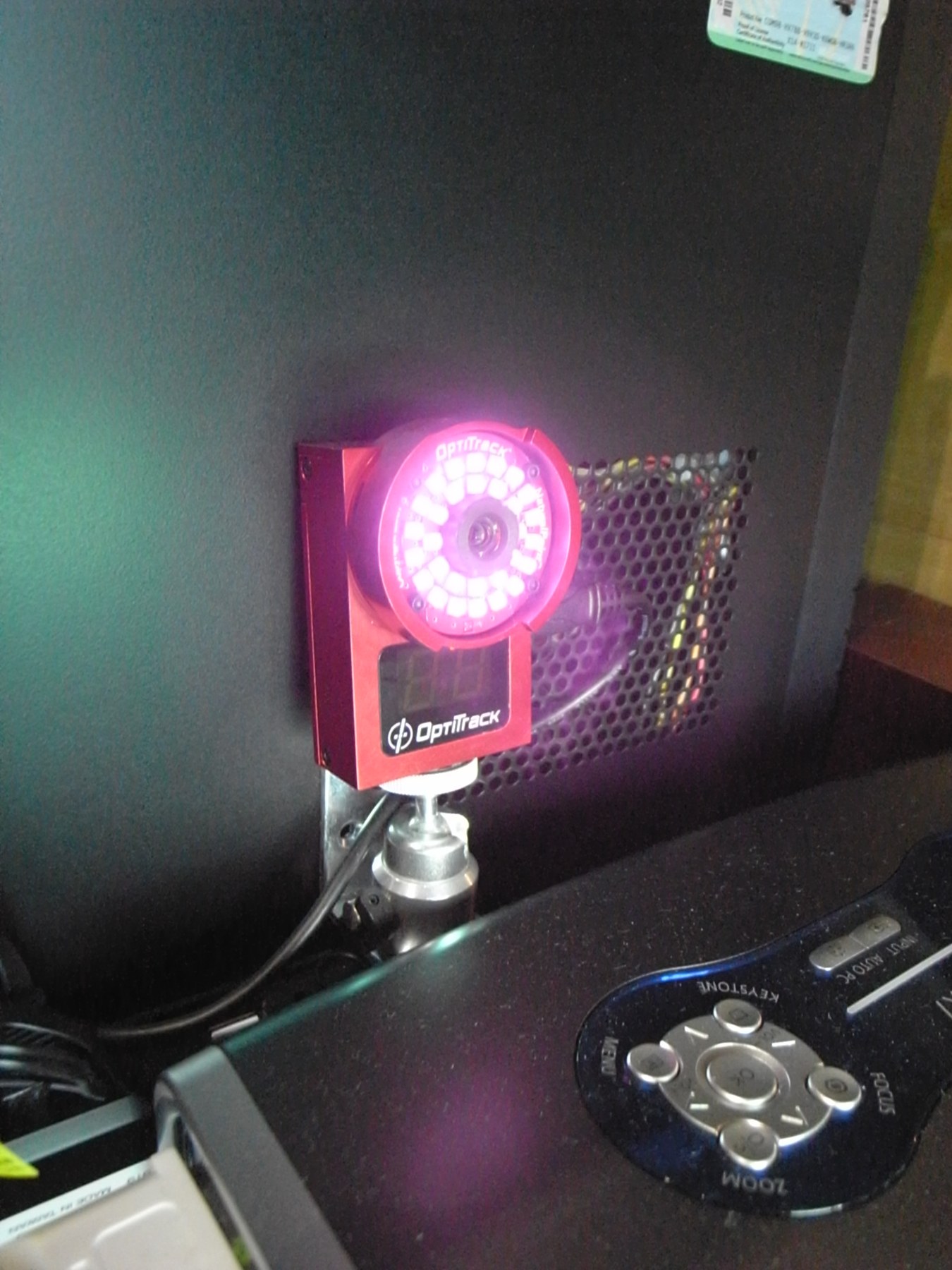 Figure 1 — An OptiTrack motion-capture camera on a stand, its ring of infrared LEDs glowing round the lens (the photographer's camera records the near infrared as violet). The light source sits on the camera,…