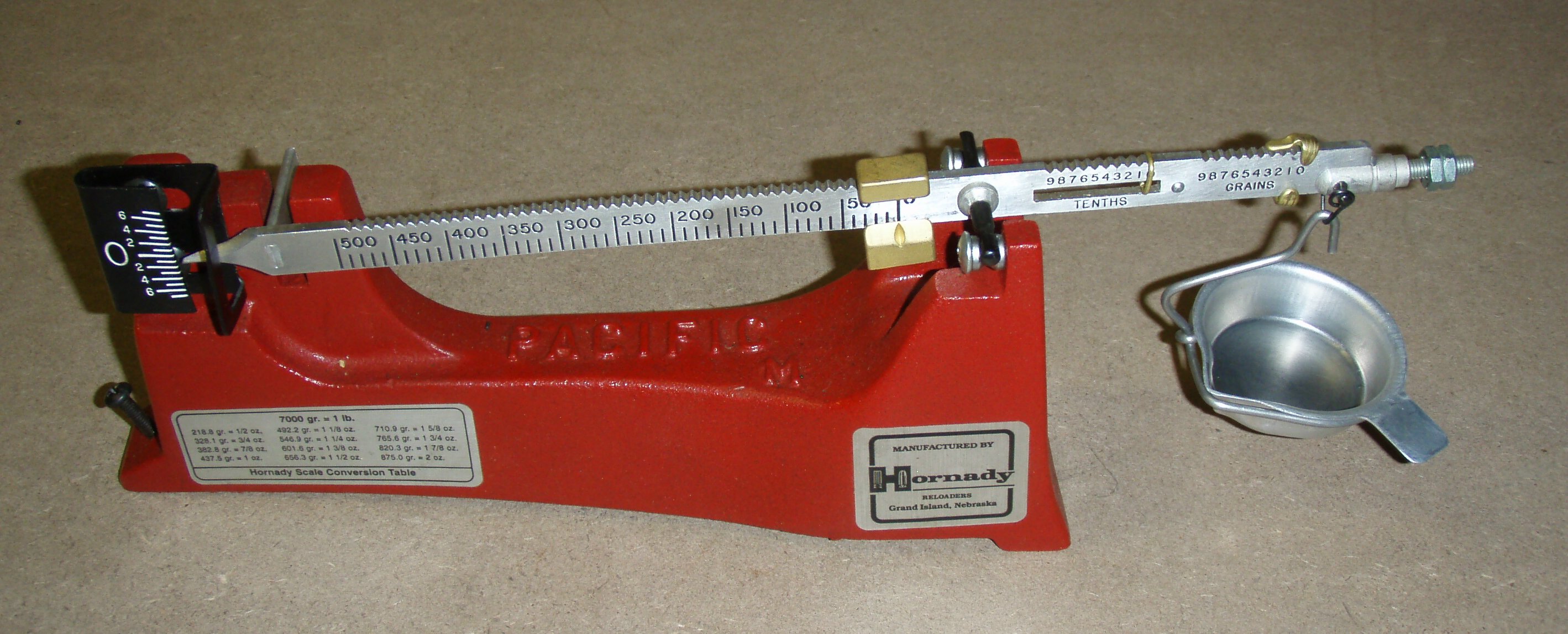 Figure 4 — A beam balance with its pan and scoop. The pointer-and-scale arrangement is what the discussion of beam scales depends on. Photograph by Arthurrh, CC BY-SA 3.0, via Wikimedia Commons (File:Powder S…